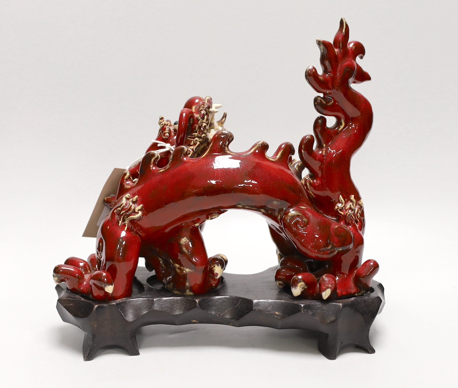 A Chinese red glazed figure of a dragon, on hardwood stand. 28cm wide